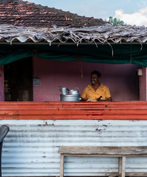 Local tea shop in Kollengode with a vendor preparing tea behind a rustic counter.